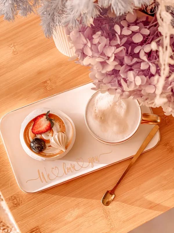A latte and a berry dessert on a tray beneath pink hydrangeas