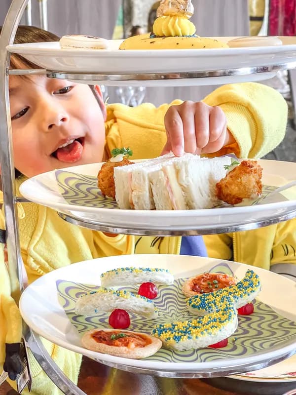A child reaching for a sandwich from a tiered afternoon tea stand
