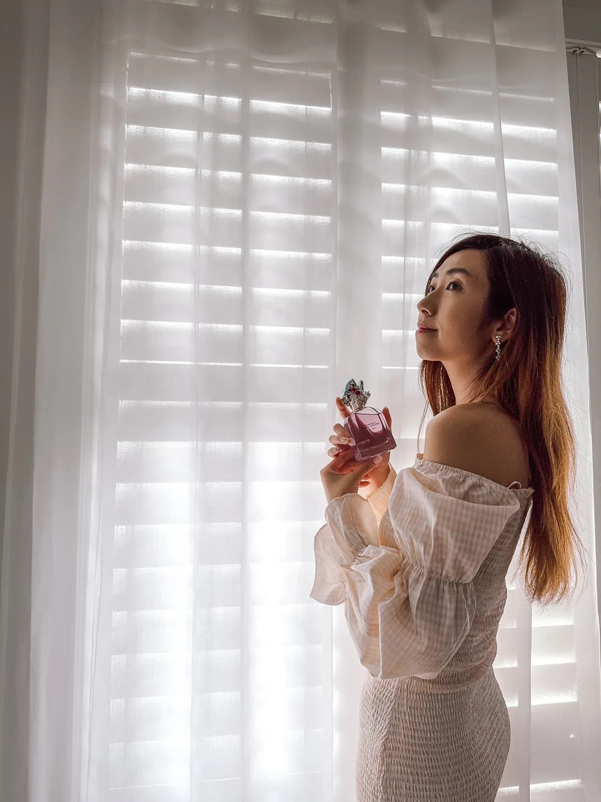 Jeannie Chow in a white off-shoulder top, standing by sheer curtains in soft window light