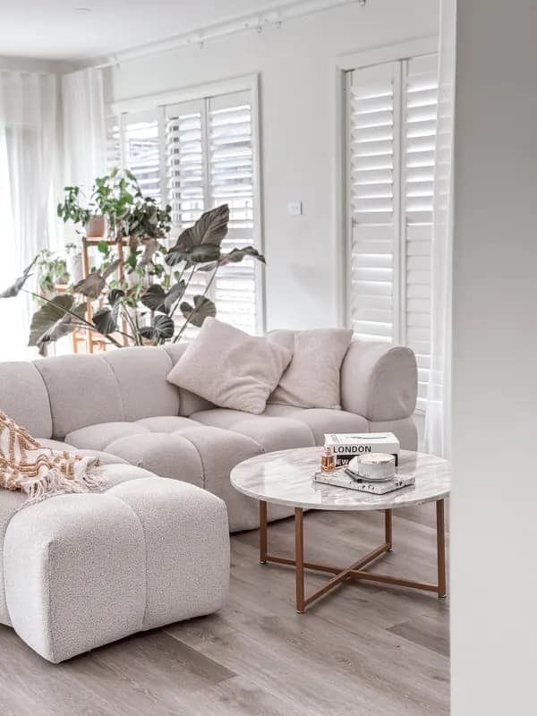 A bright living room with a modular white sofa, plantation shutters and a coffee table