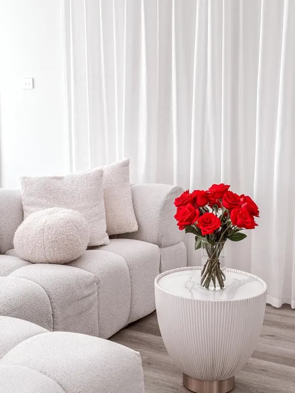 A white bouclé sofa beside a side table holding a vase of red roses