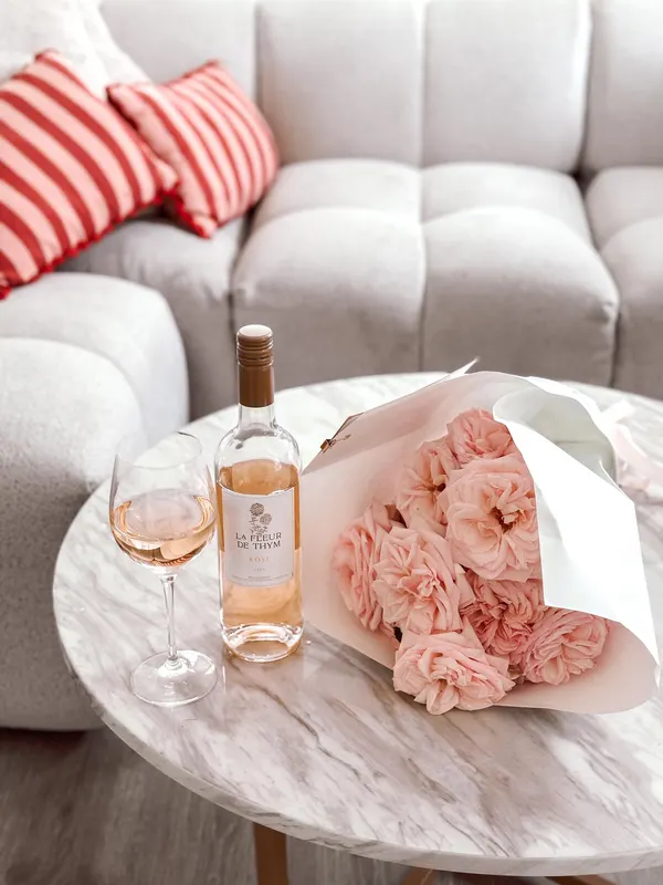 A bottle of rosé, a poured glass and a bouquet of pink roses on a marble side table