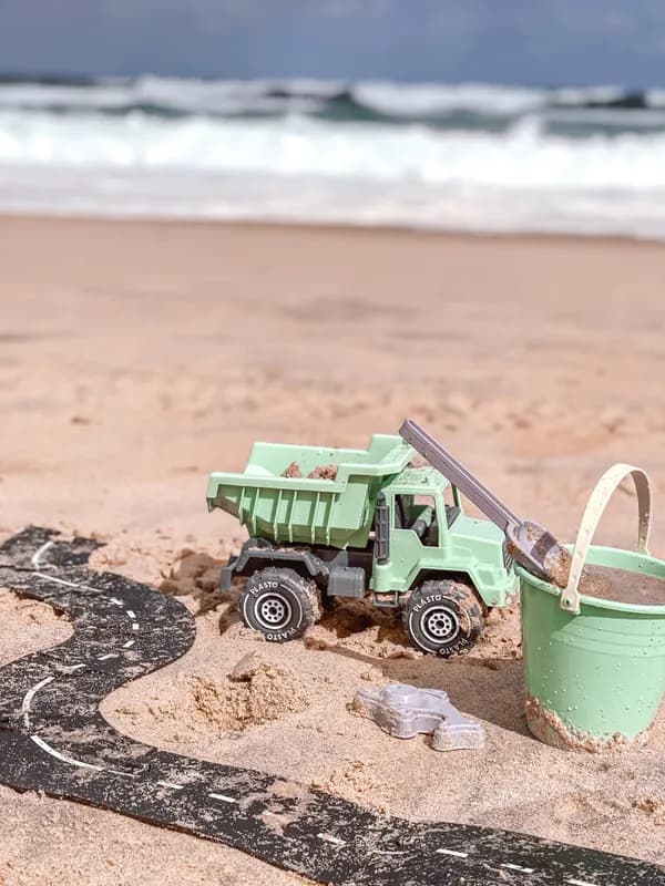 A toy dump truck on a sandy beach with waves behind